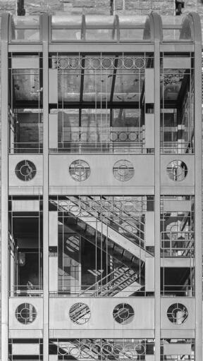 An exterior building fire escape staircase, contained in an elaborate metalwork cage, casting abstract shadows into the stairwell.