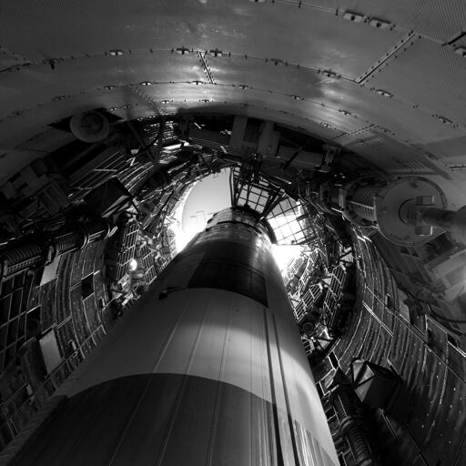 A missile pointed up inside a cramped underground silo, which is lined with retractable platforms and various apparatus.