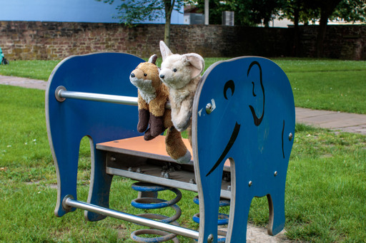 Two fox plushies (a red fox and a fennec) sitting on a blue elephant playground fixture.